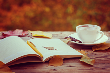 Cup of hot tea or coffee with yellow leaves and notebook on nature background. Concept autumn mood.の写真素材