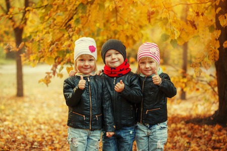 Three happy friends kids hugging and laughing in autumn park.の写真素材