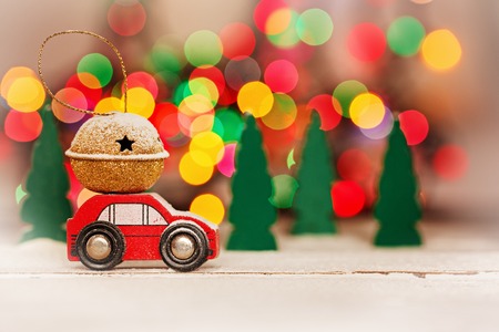 Miniature Red Car Carrying a Gift on colorful bokeh background. Holiday Merry Christmas concept.