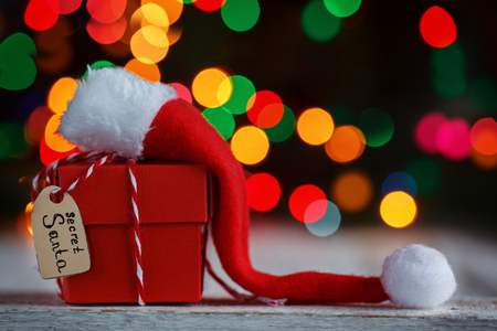 Christmas present or box for secret santa with Santa hat on colorful bokeh background.の写真素材