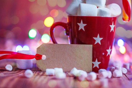 Red cup of hot cocoa with marshmallows and candy canes, with blank for text a colorful bokeh...