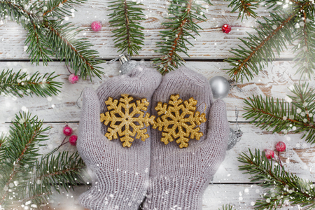 Christmas background with woman hands in mittens holding golden baubles and fir branch on white wooden tableの写真素材