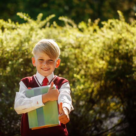 Little pupil going back to school. Child with backpack and books on first school day. Boy shows thumb up.の写真素材