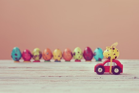 Easter holiday concept - Red toy car carrying yellow egg. Toned picture.
