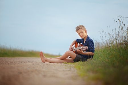 Handsome cute boy is playing on acoustic guitar sittingon road in summer dayの写真素材