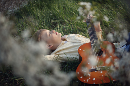 Cute boy lies on the grass with a guitar on sunset.の写真素材