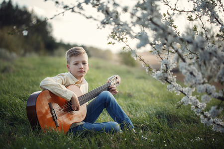 Cute boy making music playing the guitar on natureの写真素材