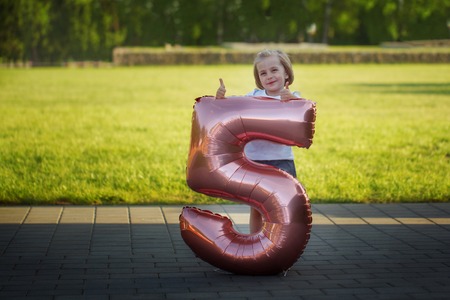Little girl with a balloon in the shape of a figure five. Birthday concept