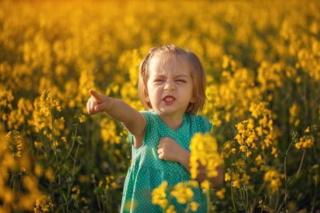 Funny little girl walking in the field of yellow flowers in a sunny summer day.