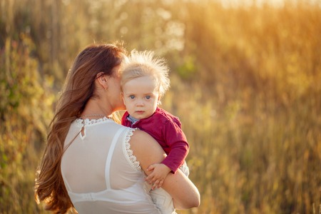 Young mother with her cute child, enjoying the sunny day over summer field. Back viewの写真素材