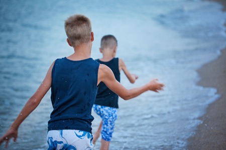Two kids boys walking on sea beach, happy best friends playing. Back view. Selective focusの写真素材