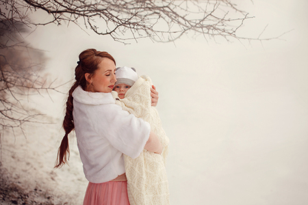 Mother holds on hands her little baby on winter walk outdoorsの写真素材