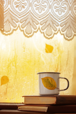 Cup of autumn tea, coffee, chocolate and yellow leaves on rainy window, copy space. Hot drink for autumn moodの写真素材