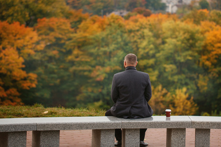Lone man sitting on the stone bench and looking at nature. Back view.の写真素材