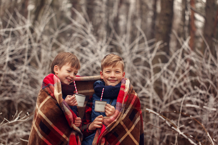 Children drink hot chocolate under warm blanket in winter forest.の写真素材