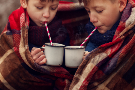 Children drink hot chocolate under warm blanket in winter forest.の写真素材