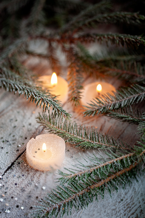 Burning candle and Christmas decoration over snow with pine branches on white wooden backgroundの写真素材