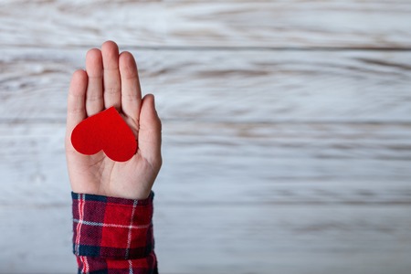Child hands holding red paper heart in hands on white wooden background. Valentines day, Mothers Day and Love concept.の写真素材