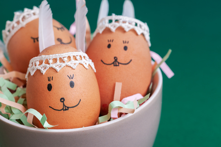 Funny easter bunnies eggs in bowl on green paper background with copy space. Happy Easter concept.の写真素材