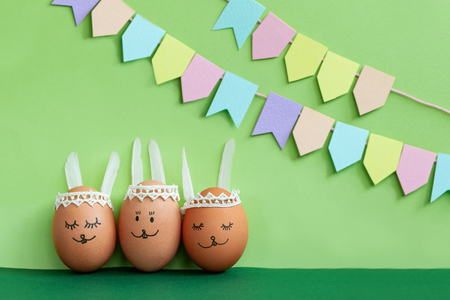 Decorated Easter egg and cute bunnys ears with colorful flags on green backgroundの写真素材