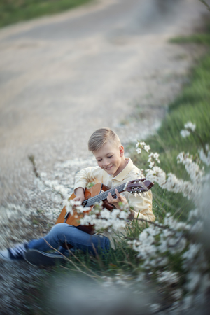 Outdoor portrait of a young teenager playing guitar and sitting on the road near spring park.の写真素材