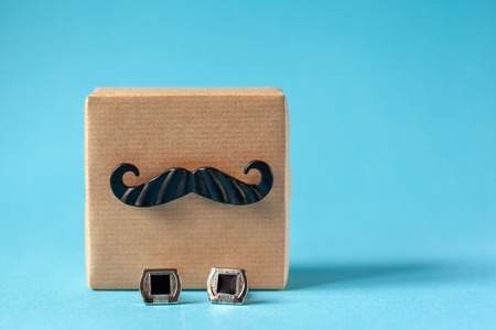 One gift box wrapped in craft paper with mustache and cufflinks on blue background. Concept Fathers Day.の写真素材