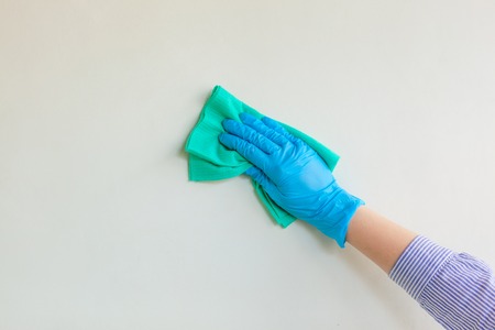 Employee hand in blue rubber protective glove wiping wall from dust with dry rag. General or regular cleanup. Commercial cleaning company. Copy space.の写真素材