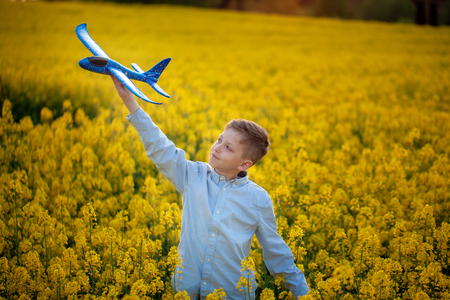 Cute boy plays with a toy airplane in the sunset and dreams of journey in summer day.の写真素材