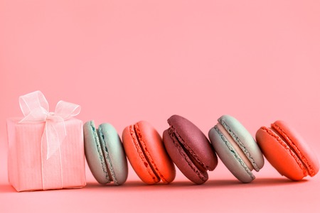Pink present and Row of french colorful macaroons, lying on coralbackgroundの写真素材
