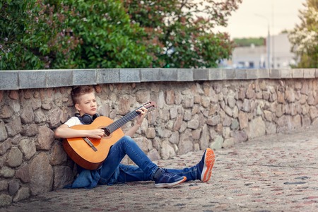 Teenager with acoustic guitar and headphones sitting in the park, outdoors.の写真素材