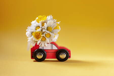 Red toy car delivering bouquet of flowers box on yellow background. Flower delivery. Happy Women's Day and Holiday conncept.の写真素材