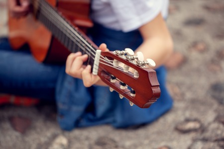 Young man holding a guitar and playing music. Focus on the head of Six-string guitarの写真素材