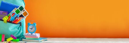 Concept back to school. Full turquoise School Backpack with stationery on table on orange...