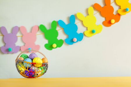 Colorful eggs in basket with handmade bunny easter garland on netural background. Concept easter.