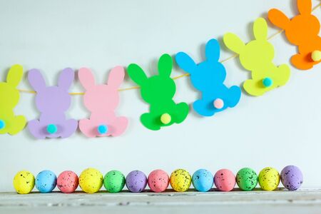 Colorful Easter eggs and handmade bunny easter garland on beige background. Happy Easter concept.の写真素材
