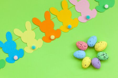 Colorful Easter eggs and handmade bunny easter garland on green background. Top view, flat lay....