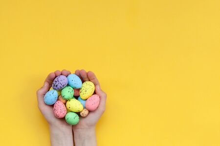 Kid's hands holding colorful painted easter eggs on yellow background. Happy Easter concept.