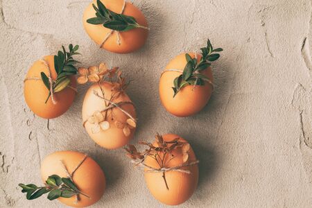 Natural eggs with bunch plant and dried flowers on grey concrete background. Eco-friendly Easter...