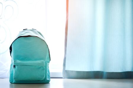 Blue school backpack on table over children room interior in sunny day. Back to school concept.