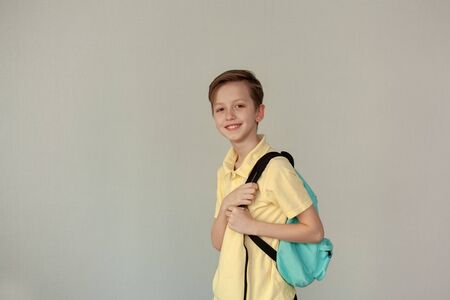 Portrait of smiling schoolboy wearing casual clothing and backpack smiling at camera over netural background, copy space. Back to schooolの写真素材