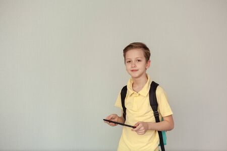 Portrait of schoolboy wearing backpack using tablet computer, look at camera over netural background, copy space. Back to schoolの写真素材