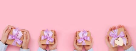 Kid's hands holding gift box wrapped in craft paper and tied with bow on pink background. Concept...