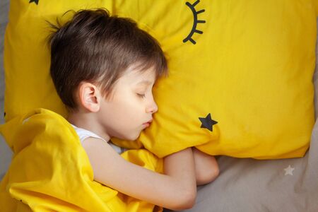Portrait Sleeping child on soft light background. Top view of little boy sleeping in yellow bed.