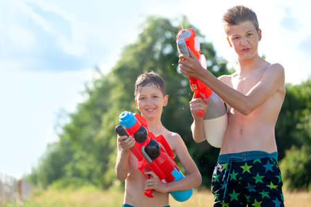 Two Kids playing with water guns outdoors. Cute boys spraying water from a gun in backyard. Songkran thailand festivalの写真素材