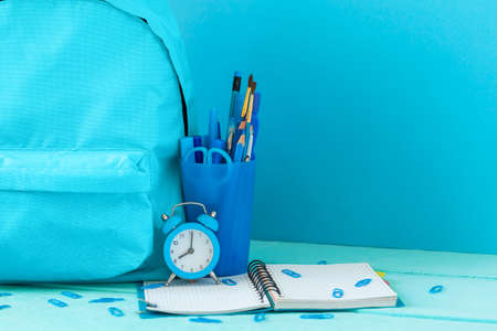 Backpack prepared with schoolstationery supplies and alarm clockfor the back to school. Concept blue monochrome color.の写真素材