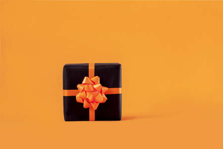 Wrapped handmade present box in black paper with bow on orange background. Halloween and Birthday concept.の写真素材
