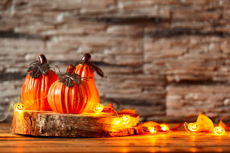 Holiday decoration with decorative ceramic pumpkins with decoration light Garland of glowing on wooden table. Halloween background.の写真素材