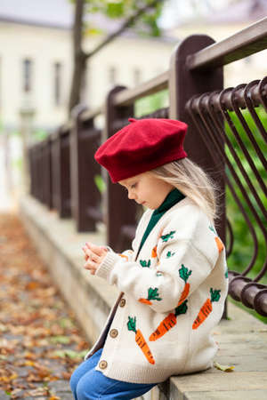 Beautiful blonde girl in sunny autumn park. Child playing in park at autumn. Autumn mood.の写真素材