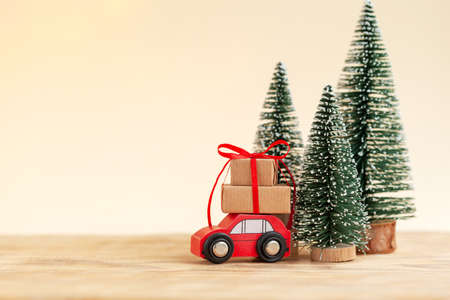 Red toy car with Stack of Christmas gift boxes aginst netural background with christmas trees. Holiday greeting card.の写真素材
