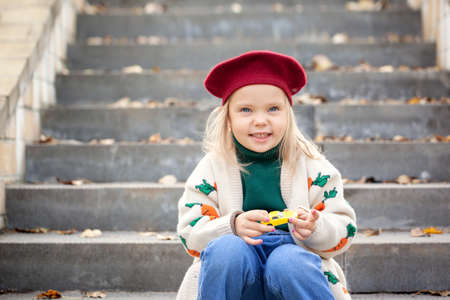 Autumn happy little child in autumn park. Pretty kid girl in a beret and a sweater in autumn warm sunny weather.の写真素材